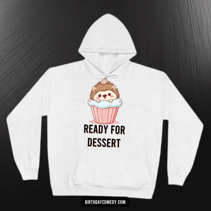 Funny Hoodie: A delightful image of a happy hedgehog peeking from behind a large cupcake, offering warmth and a dose of sugary delight.