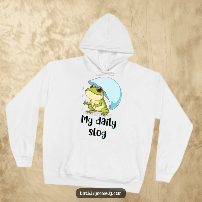 Funny frog hoodie showing a determined frog comically pushing a giant raindrop uphill, perfect for cozy, humorous motivation.