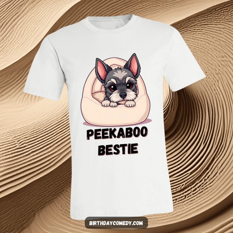 Funny t-shirt showcasing a schnauzer puppy peeking from a cozy dog bed, its expressive eyes inviting a playful interaction.