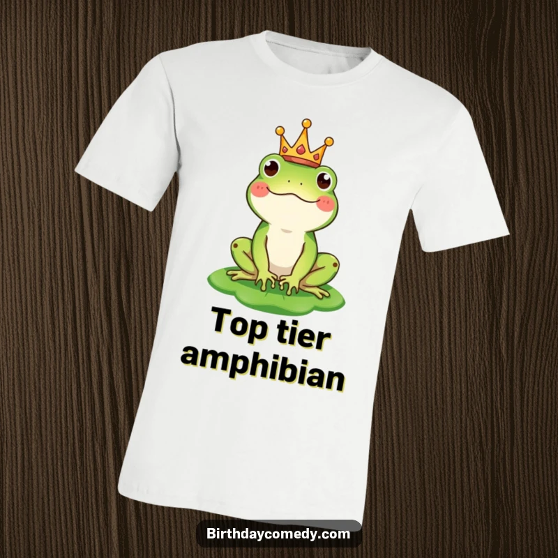 Funny t-shirt depicting a happy frog wearing a tiny crown and creatively balancing a lily pad as a hat, exuding royal charm.
